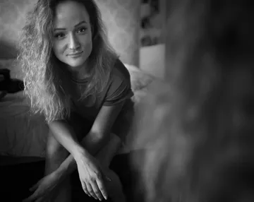 Woman sitting, looking in mirror, bedroom context.