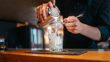 Barkeeper gießt Cocktail durch Sieb in Bar.
