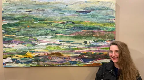 Woman smiling beside abstract landscape painting.