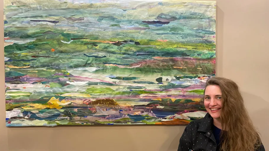 Woman smiling beside abstract landscape painting.