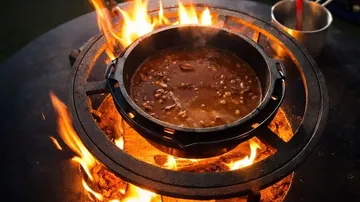 Pot cooking stew over open fire outdoors.