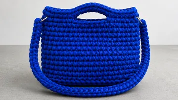 Blue crocheted handbag on gray surface.