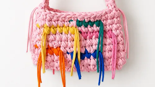 Rosa geflochtene Handtasche mit bunten Quasten.