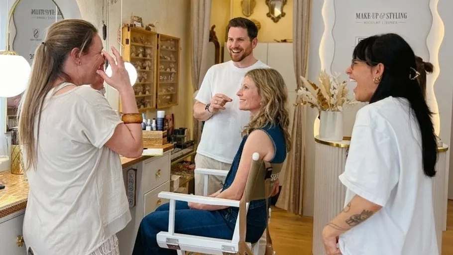 Frau sitzt, andere lächeln im Makeup-Studio.