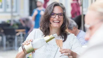 Frau gießt Sekt draußen fröhlich ein.