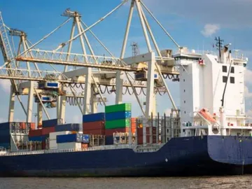Containerschiff lädt Waren unter Kransystem in einem Hafen.