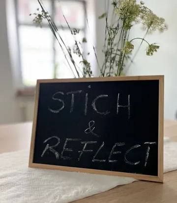 Tafel mit 'STICH & REFLECT' in gemütlichem Raum.