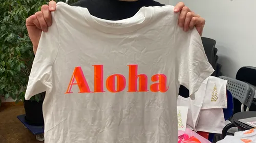 Person hält T-Shirt mit 'Aloha' innen.