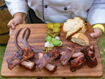 Holzbrett mit gegrilltem Fleisch und Beilagen wird gehalten.