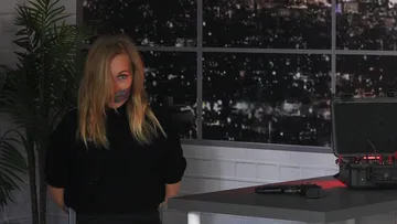 Person standing, gagged, in a dark room.