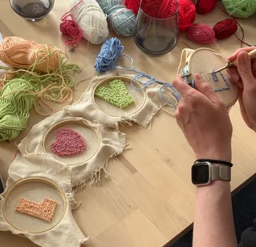 Hände sticken Stoff mit buntem Garn auf Tisch.