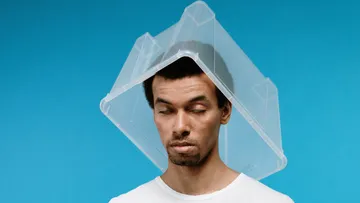 Mann mit Plastikbox über Kopf, blauer Hintergrund.