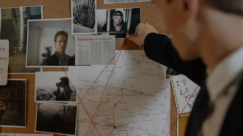 Detective points at photos on cork board.