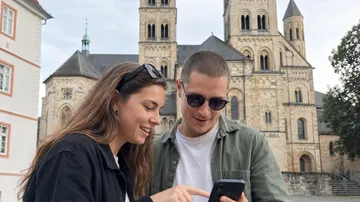 Zwei Personen schauen auf Handy vor Kathedrale.