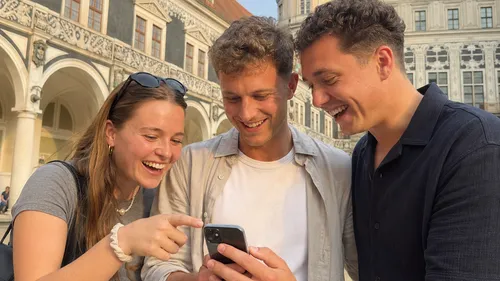 Three people smiling at smartphone outdoors.