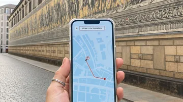 Hand holds phone with map, mural in background.