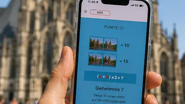 Hand hält Handy mit Rätsel, Kathedrale im Hintergrund.