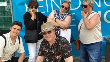 Gruppe posiert vor blauem Banner im Freien.