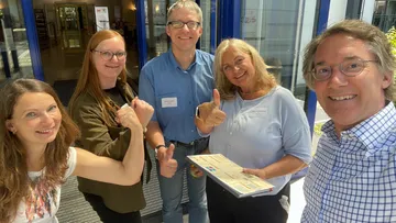 Gruppe von fünf lächelnden Menschen draußen.