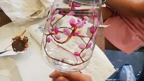 Weinglas mit rosa Blumen bemalt, Hand haltend.