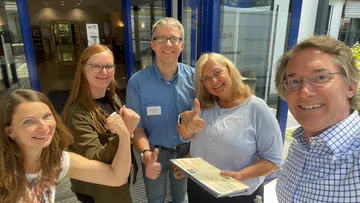 Group smiling, giving thumbs up, indoors.
