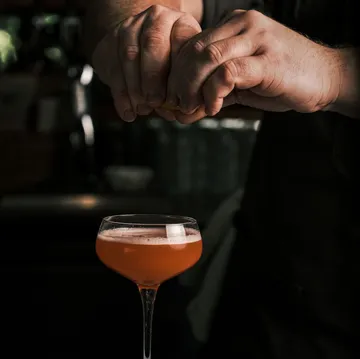 Hände pressen Zitrone über Cocktailglas.