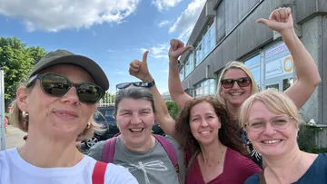 Fünf Personen lächeln vor einem Gebäude.