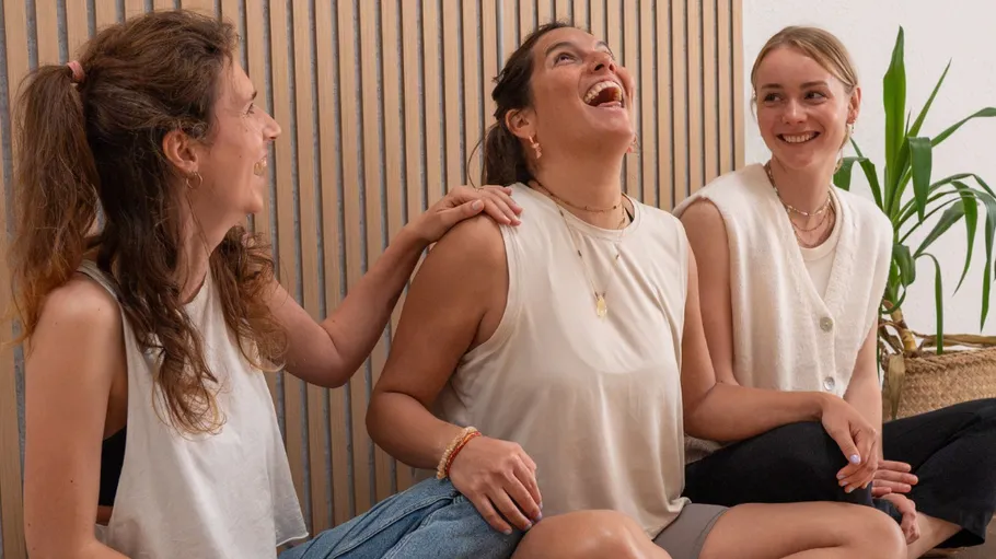 Three women laughing indoors, sitting together.