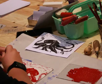 Person creating print on wooden table.