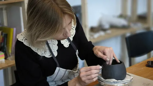 Woman sculpting clay pot at workshop.