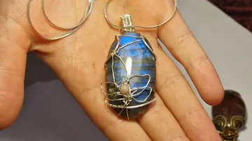 Hand hält blauen Draht-umwickelten Edelsteinanhänger.