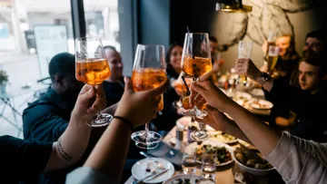 Hands toast with drinks at restaurant table.