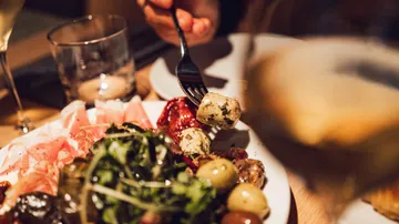 Person eating antipasto with fork, dinner table.