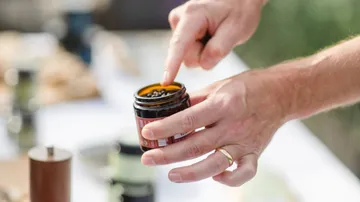 Hand trägt Balsam aus einem kleinen Glas auf.