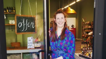 Frau öffnet Tür eines kleinen Ladens.