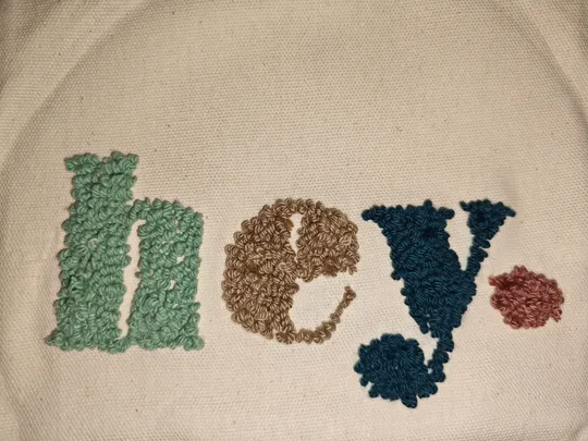 Stickerei mit 'hey' auf weißem Stoff.