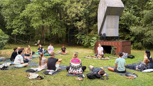 Group meditating outdoors near wooden sculpture.