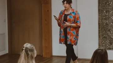 Person spricht zu sitzendem Publikum drinnen.