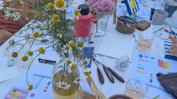 Flowers in vase on cluttered art table.