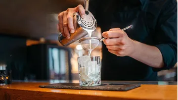 Bartender pouring cocktail through strainer into glass.