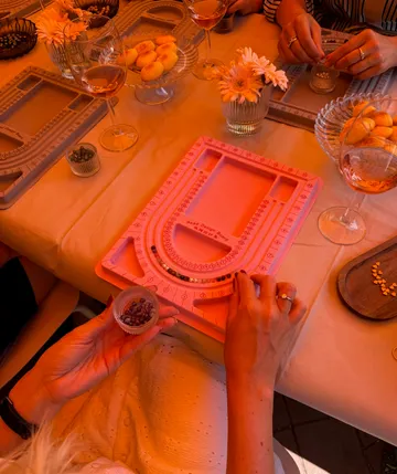 Hands arranging beads on design board.