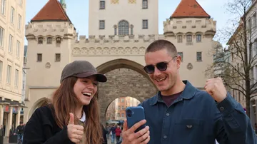 Two people cheering with phone by historic gate.