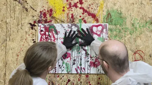 Zwei Personen malen auf bespritzter Leinwand.