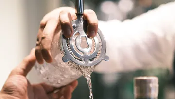 Bartender straining cocktail into a glass.