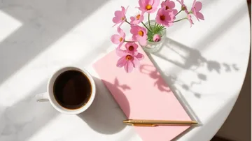 Kaffee, Notizbuch und Blumen auf sonnigem Tisch.