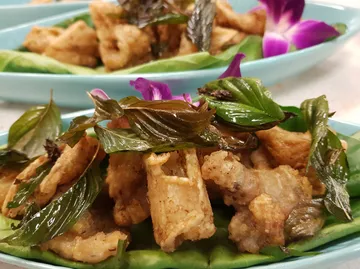 Frittiertes Essen mit Basilikumblättern auf Teller.