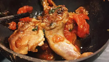 Gebratenes Hähnchen mit Tomaten in einer Pfanne.