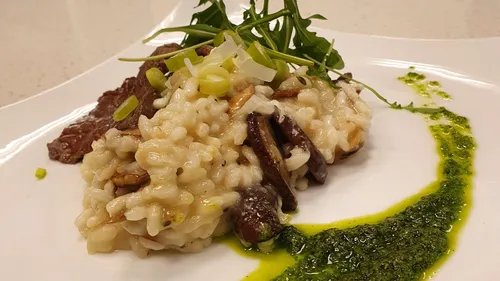 Pilzrisotto mit Rucola auf einem Teller dekoriert.