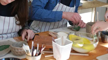 Menschen fertigen Keramik am Workshop-Tisch an.