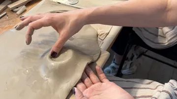 Hände formen Ton auf einem Tisch.